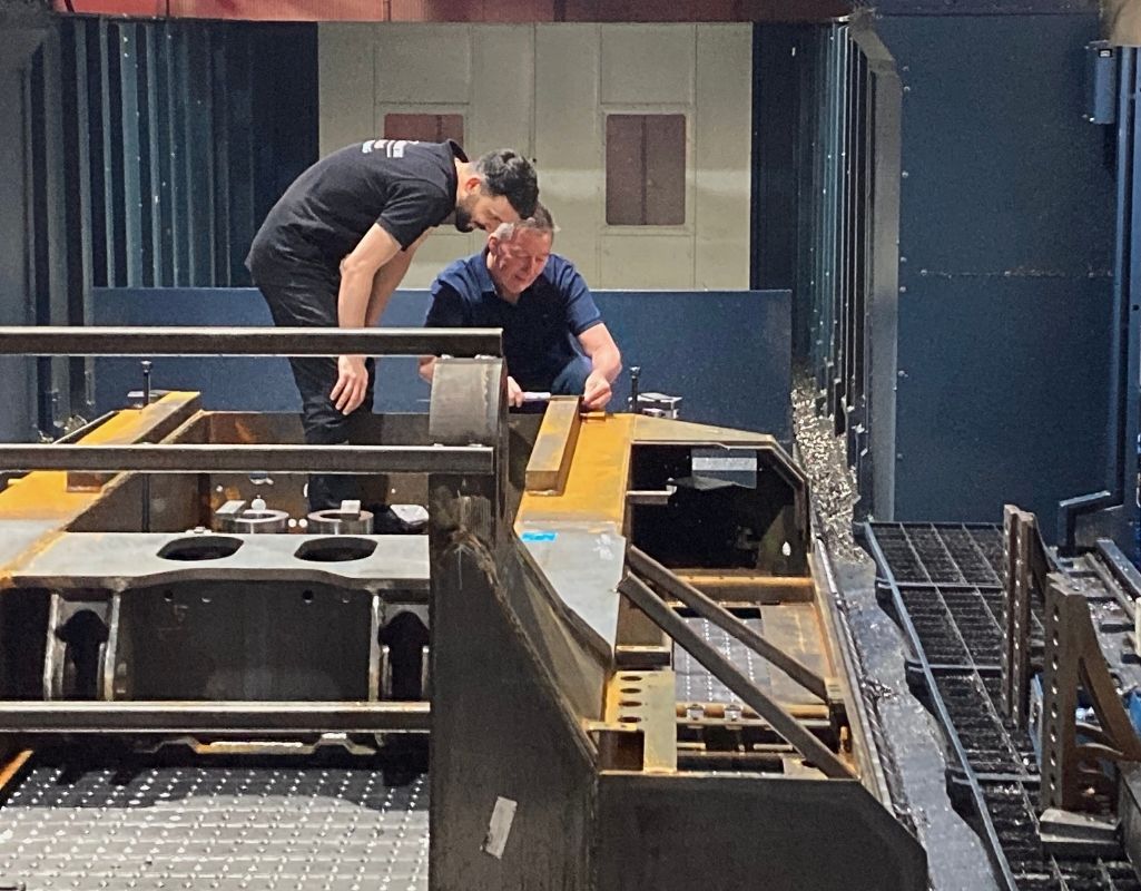 Michael von Briel steht mit einem Arbeiter an einer Fräsmaschine und erklärt ein neues Vorgehen.